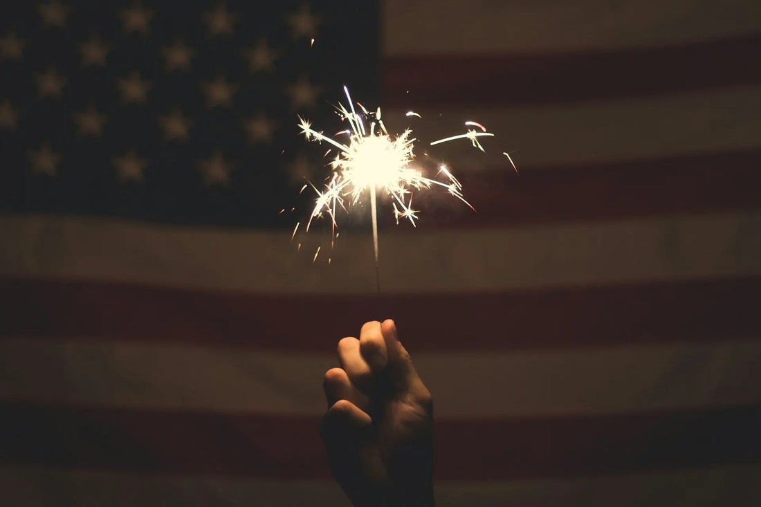Fireworks light up the night sky with American flags waving, celebrating the 4th of July.