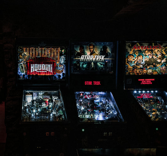 Three themed pinball machines in a trivia night setting, featuring Houdini, Star Trek, and Metallica designs, creating an engaging and nostalgic vibe for participants.